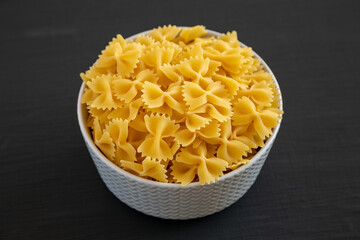 Raw Organic Farfalle Pasta in a Bowl on a black background, side view.