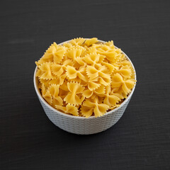 Raw Organic Farfalle Pasta in a Bowl on a black background, low angle view.