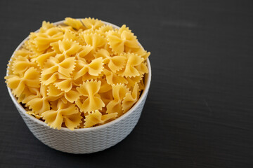 Raw Organic Farfalle Pasta in a Bowl on a black background, side view. Space for text.