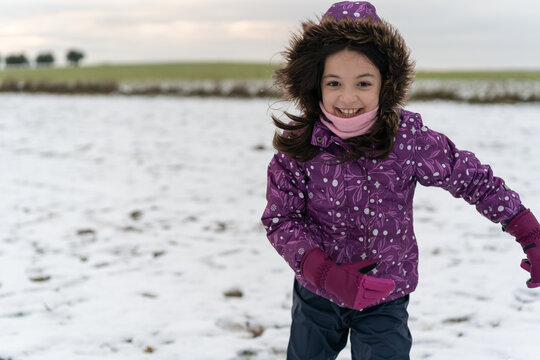 Girl playing happily in the snow in a field with olive trees