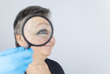 Senior woman at the reception of a facial plastic surgeon. Consultation on the removal of age wrinkles on the face. Doctor shows what procedures he will do. Mimic wrinkles. Magnifying glass in hands