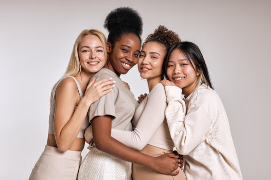 Portrait of four happy beautiful diverse young women with perfect skin posing for camera while standing isolated over white studio background. Attractive ladies in casual clothes are friends