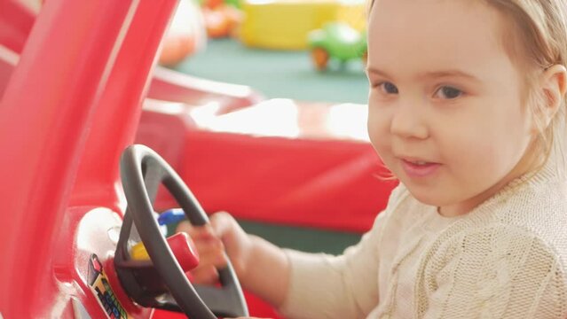 child girl plays with car, rides, drives. Children's play center, room, kindergarten. Happy and cheerful. steering wheel