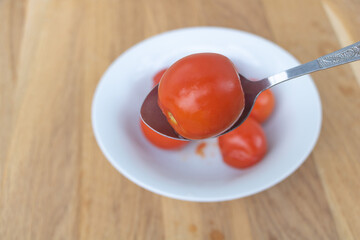 Close up shot of marinated tomatoes in a white plate with wooden background - A spoon with tomatoes
