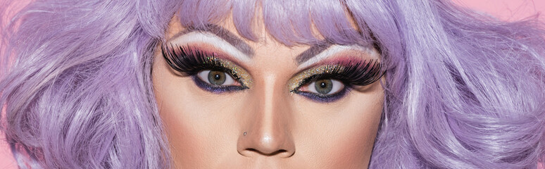Naklejka premium partial view of drag queen in purple wig looking at camera, banner.