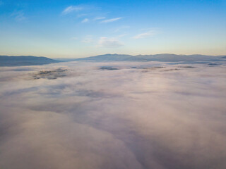 Obraz na płótnie Canvas Flight over fog in Ukrainian Carpathians in summer. A thick layer of fog covers the mountains with a solid carpet. Mountains on the horizon. Aerial drone view.