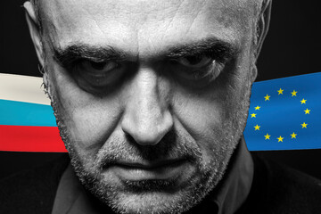foto in b/n di un uomo con espressione seria e dietro le bandiere della Russia e dell'europa
