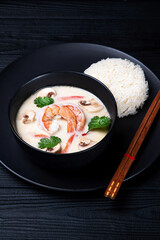 High angel view of coconut milk soup with shrimps Tom Kha Gai in a black bowl with chopsticks.