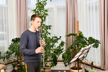 A young guy plays the clarinet from notes. Learning music at home.