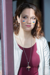 ritratto di una ragazza con i colori dell'Ucraina disegnata sul viso che guarda fuori dalla finestra