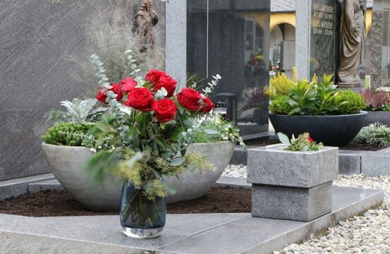 Mit Blumen geschmückte Gräber an einem österreichischen Friedhof, im Vordergrund eine Blumenschale mit roten Rosen, Tod, Sterben, Bestattung, Trauer, Friedhofsgestaltung