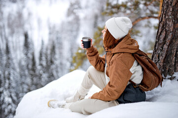 Calm redhead caucasian woman sit on snow on top of mountains relaxing, drinking hot tea from thermos, having rest after hike, travel, trip, adventure. inspiration, magnificent view landscape
