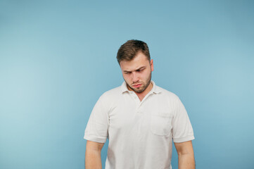 Obraz premium Portrait of upset man with bristles on blue background, wearing white t-shirt, head down from failure.