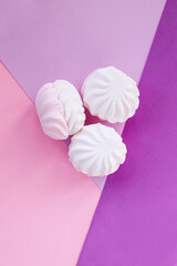 Three airy soft marshmallows on a multi-colored creative flatlay background. Stylish and geometric design of sweets and confectionery. Delicate marshmallows on pink and purple background