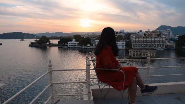 Beautiful Indian female enjoying sunset while sitting near lake Pichola at Udaipur city, Rajasthan, India. Woman relaxing during holidays. Sunset at Udaipur city. People enjoying holidays