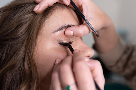 Make-up artist applies eyeliner to the girl's upper eyelid with a brush