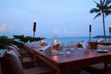 Outdoor restaurant table set for dinner with candles and torches on tropical beach