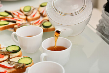 Tea leaves are poured into a cup for drinking tea with sandwiches.