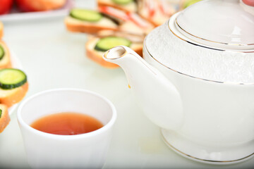 A white cup with tea and a teapot in the kitchen at the table.