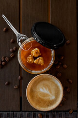 Takeaway coffee in a paper cup and a delicious dessert with salted caramel in a glass jar on a wooden one on a wooden table. Close-up. Selective focus. Soft blurred background. Top view.