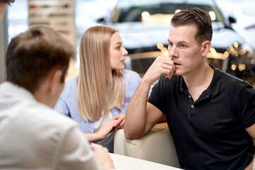 rear view on skilled confident male manager talking to clients, explaining rules for buying car, married family couple sit listening to consultant, have talk discussion. in modern car dealership