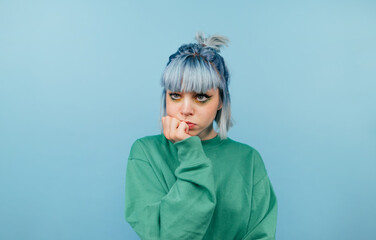 Pensive casual girl with blue hair isolated on blue background, looks away and thinks