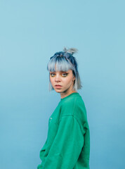 Portrait of a beautiful woman with blue hair posing at camera on a blue background with a serious...