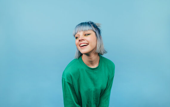 Attractive lady with colored hair with a smile on her face isolated on a blue background in a green sweater looking aside