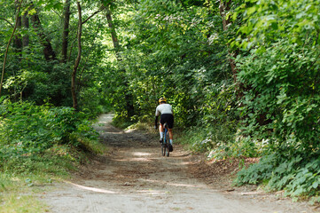 Fototapeta premium Cyclist rides on a dirt road on a bicycle, view from the back.