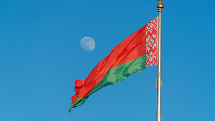 State flags of the Republic of Belarus are waving in the wind on blue sky with full moon...