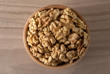 Bowl full of peeled walnuts on a wooden background,top view