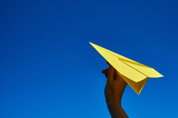 Paper yellow plane in the hands against the blue sky. Taking flight! Travel concept