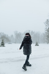 Full-length portrait of a stylish lady in casual clothes on a walk on a snowy winter day, having fun in the snowfall. Vertical