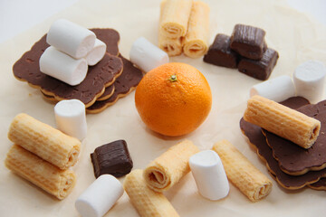 the choice of healthy or harmful sweets. chocolates, cookies, waffles, marshmallows and tangerine on parchment paper