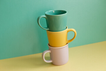Stack of mug cups on yellow table. green wall background. home interior