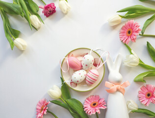 Layout of easter table decoration with easter bunny and pink eggs on roses plate, with pink daisy flowers and white tulips. Easter bunny with ribbon. Celebration layout or card. Minimalist table decor