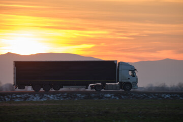 Semi-truck with cargo trailer driving on highway hauling goods in evening. Delivery transportation and logistics concept