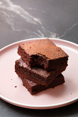 Slices of brownie dessert on a dark background on a pink plate

