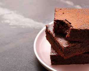 Slices of brownie dessert on a dark background on a pink plate
