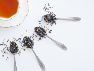 A cup of tea on a saucer. Dry black tea mixed with herbs for brewing is poured into spoons,...