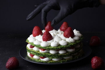 Step-by-step preparation of green cake from spinach and strawberries. Final step. Hand confectioner in black gloves decorating cake