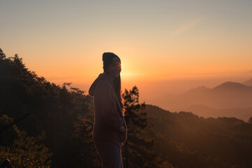 Happy asian woman wearing beanie standing with sunrise over mountain in the morning