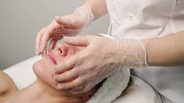 Face massage at spa salon. Doctor hands. Pretty female patient. Beauty treatment. Healthy skin procedure. Young woman head. Scrub rejuvenation. Facial dermatology mask. Detox therapy video