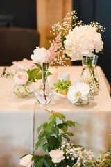 Coziness and style. Modern event design. Table setting at wedding reception. Floral compositions with beautiful flowers and greenery, candles, laying and plates on decorated table.