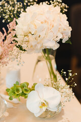 Coziness and style. Modern event design. Table setting at wedding reception. Floral compositions with beautiful flowers and greenery, candles, laying and plates on decorated table.