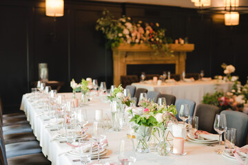 Coziness and style. Modern event design. Table setting at wedding reception. Floral compositions with beautiful flowers and greenery, candles, laying and plates on decorated table.