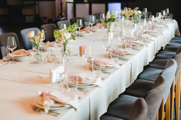 Coziness and style. Modern event design. Table setting at wedding reception. Floral compositions with beautiful flowers and greenery, candles, laying and plates on decorated table.