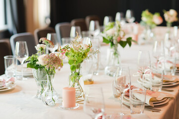 Coziness and style. Modern event design. Table setting at wedding reception. Floral compositions with beautiful flowers and greenery, candles, laying and plates on decorated table.
