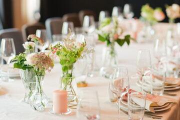 Coziness and style. Modern event design. Table setting at wedding reception. Floral compositions with beautiful flowers and greenery, candles, laying and plates on decorated table.