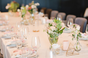 Coziness and style. Modern event design. Table setting at wedding reception. Floral compositions with beautiful flowers and greenery, candles, laying and plates on decorated table.